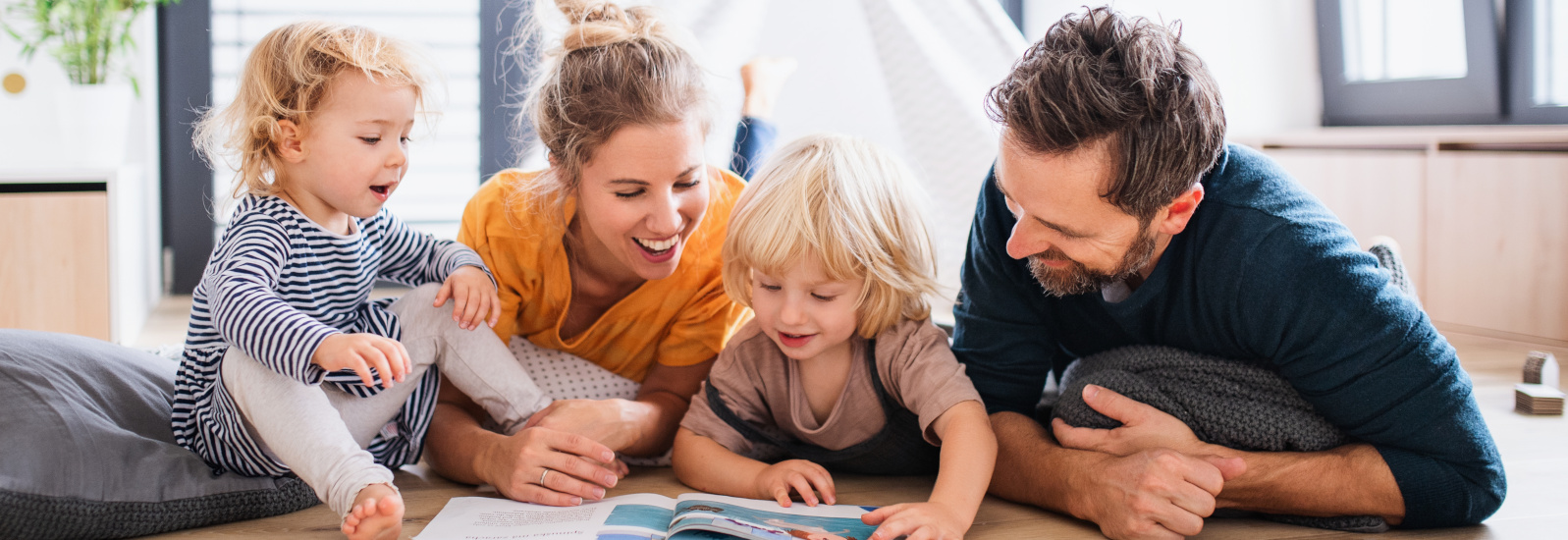 Bild einer vierköpfigen Familie, die gemeinsam auf dem Boden liegend ein Buch lesen